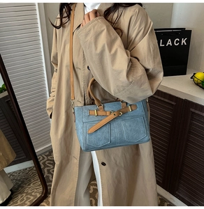 Detail of blue denim tote bag with brown leather straps and vintage front pockets