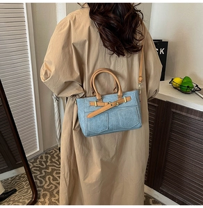 Detail of blue denim patchwork tote with brown leather handles and adjustable strap