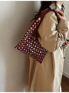 Sac croissant rouge foncé clouté d'argent porté par un mannequin en trench-coat beige