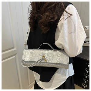 Détail du sac baguette argenté à motif crocodile avec boucle de nœud doré élégante