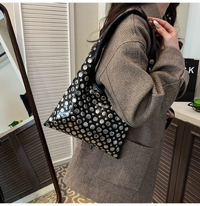 Detail of black triangular bucket bag with silver studs worn by a model in a warm room