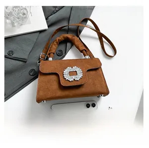 Detail of suede crossbody bag with rhinestone buckle and adjustable strap over a magazine