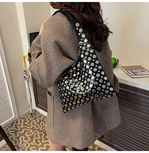Detail of glossy black hobo bag with silver studs worn by a model in wool coat