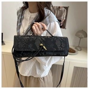Détail du sac noir aspect serpent avec boucle dorée en nœud et texture gaufrée chic