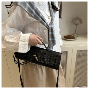 Détail de la texture cuir crocodile et du fermoir en T doré sur le sac noir chic