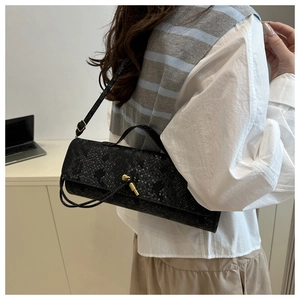 Détail latéral du sac baguette noir à motif crocodile avec fermoir métallique doré chic