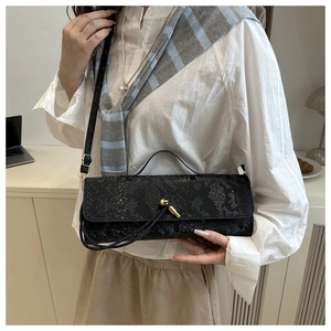 Détail d'un sac à bandoulière noir texture crocodile avec fermoir doré sur un mannequin