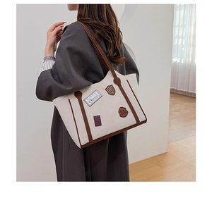 Detail of canvas tote bag with retro patches and brown leather straps on model