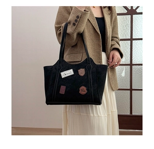 Detail of black tote bag with vintage patches styled with a brown blazer and white skirt