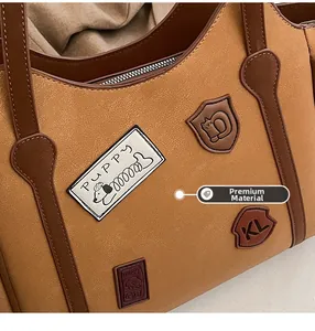 Detail of premium textured leather tote bag featuring vintage badges and metallic zipper