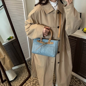Blue denim tote bag with brown leather straps and gold buckles styled on a model