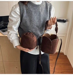 Detail of dark brown suede bucket bag with petal-shaped top and woven handle on a model
