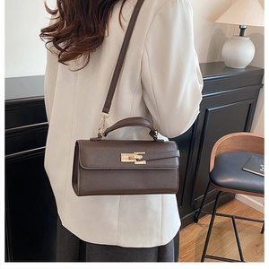 Sac à main en cuir marron foncé avec fermoir tournant doré porté sur un blazer blanc