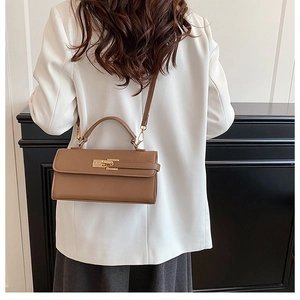 Brown leather crossbody bag with gold rotating lock shown on a model in white blazer