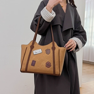 Vintage camel leather tote bag with badge patches shown on a model arm for daily use