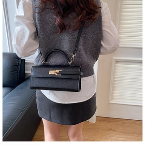 Détail d'un sac à main noir en cuir texturé avec boucle dorée porté par le mannequin