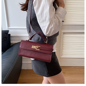 Sac à main en cuir grainé bordeaux avec boucle dorée porté par un mannequin en vue