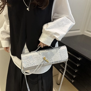 Sac baguette argenté à texture crocodile avec boucle dorée présenté en porté main élégant