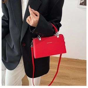 Detail of red textured leather crossbody bag showing silver hardware and fashion text