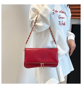 Detalle de bolso bandolera de piel roja con cadena dorada y doble cremallera decorativa