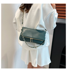 Detalle de un bolso de cadena en cuero verde oscuro con herrajes dorados en un modelo
