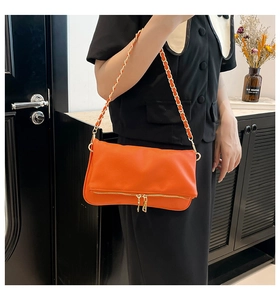 Detalle del bolso de hombro naranja brillante con cremalleras dobles y correa de cadena