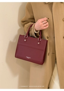 Détail d'un sac carré bordeaux texturé avec boucles argentées tenu par un mannequin