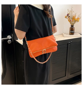 Detalle de un bolso de hombro en cuero naranja brillante con cadena dorada en una modelo
