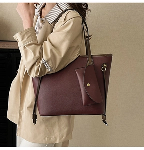 Détail du sac cabas bordeaux en cuir litchi avec porte-monnaie sur un manteau beige