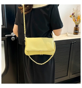 Detalle de bolso bandolera amarillo de cuero con cadena trenzada y cierre de doble cremallera