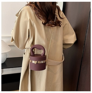 Detail of dark purple cylindrical acrylic evening bag with gold handle and chain strap