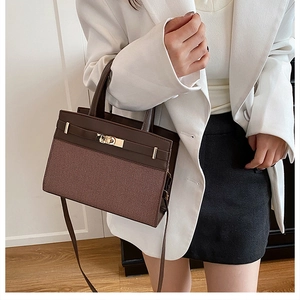 Detail shot of a brown patchwork handbag with gold metal lock on a white suit model