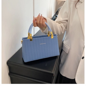 Close-up of blue woven textured handbag with golden hardware and fashion lettering