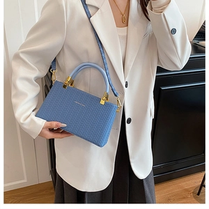 Detail of blue woven texture handbag with golden hardware and round handle on white blazer