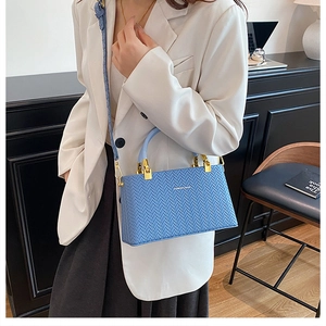 Detail of light blue box bag with woven texture and gold hardware on white blazer
