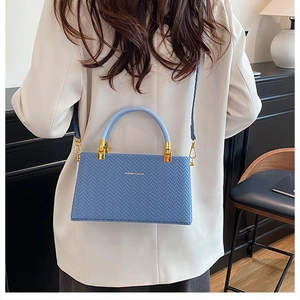 Close-up of blue woven texture handbag with golden hardware worn by a model