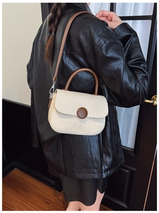 Detalle del bolso bandolera de lona beige con acabados de cuero marrón y metal