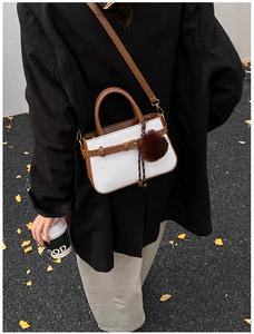 Close-up of woven bucket bag with brown leather strap and decorative fur ball charm