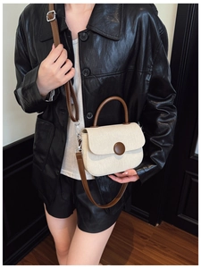 Detail of a minimalist cream woven crossbody bag with brown leather handles on a model