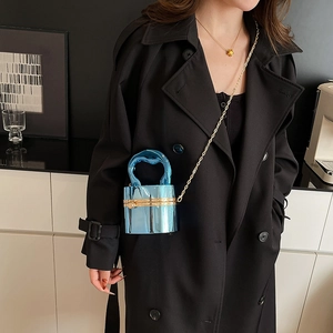 Blue metallic cylinder mini crossbody bag with gold chain and fluid handle on black coat