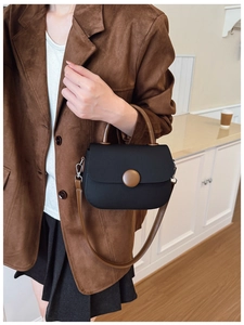 Vue détaillée du sac à main noir avec boucle marron et poignée cylindrique sur un modèle