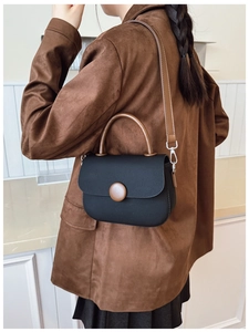Detail of a black and brown saddle bag showing a large round buckle and leather handle