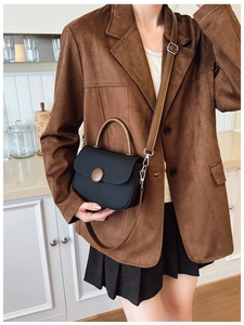 Detalle de bolso bandolera negro con asa marrón sobre una chaqueta de ante