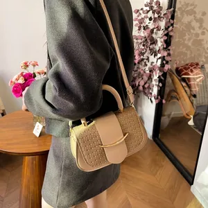 Detail of a woven beige and coffee crossbody bag with a curved gold metal trim