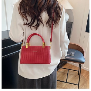 Detail view of red woven texture box bag styled with a white blazer in a warm indoor setting