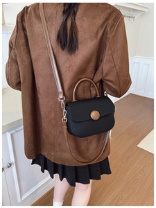 Detail view of a black matte crossbody bag with brown circular decorative buckle on a model