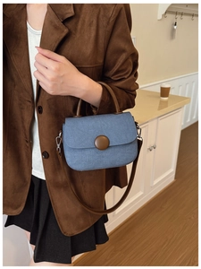 Detalle del bolso de hombro en denim azul con gran hebilla marrón y asas de cuero