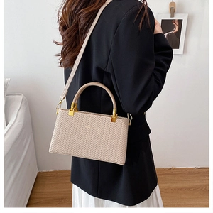 Detail of beige woven texture handbag with gold hardware worn over a black blazer