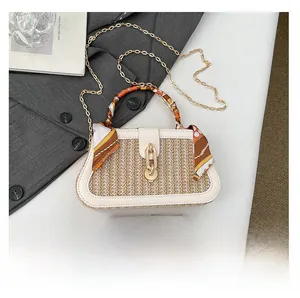 Detail of woven straw box bag with silk scarf handle and phone for size reference