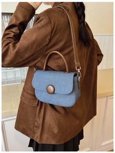 Blue denim saddle bag with brown leather strap shown on a model in a warm indoor setting